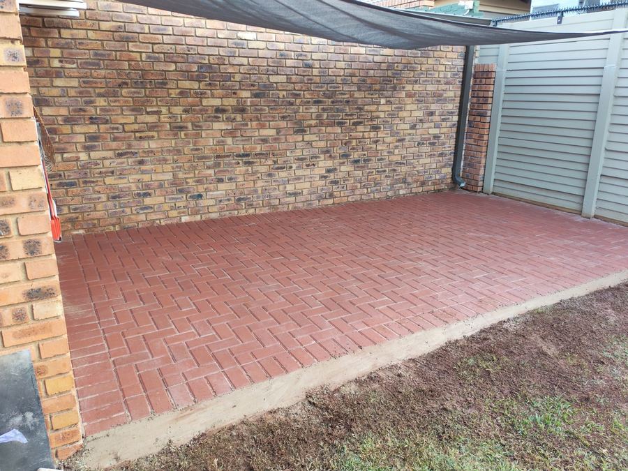 Herringbone-pattern brick patio paving installed against a face-brick wall in Pretoria